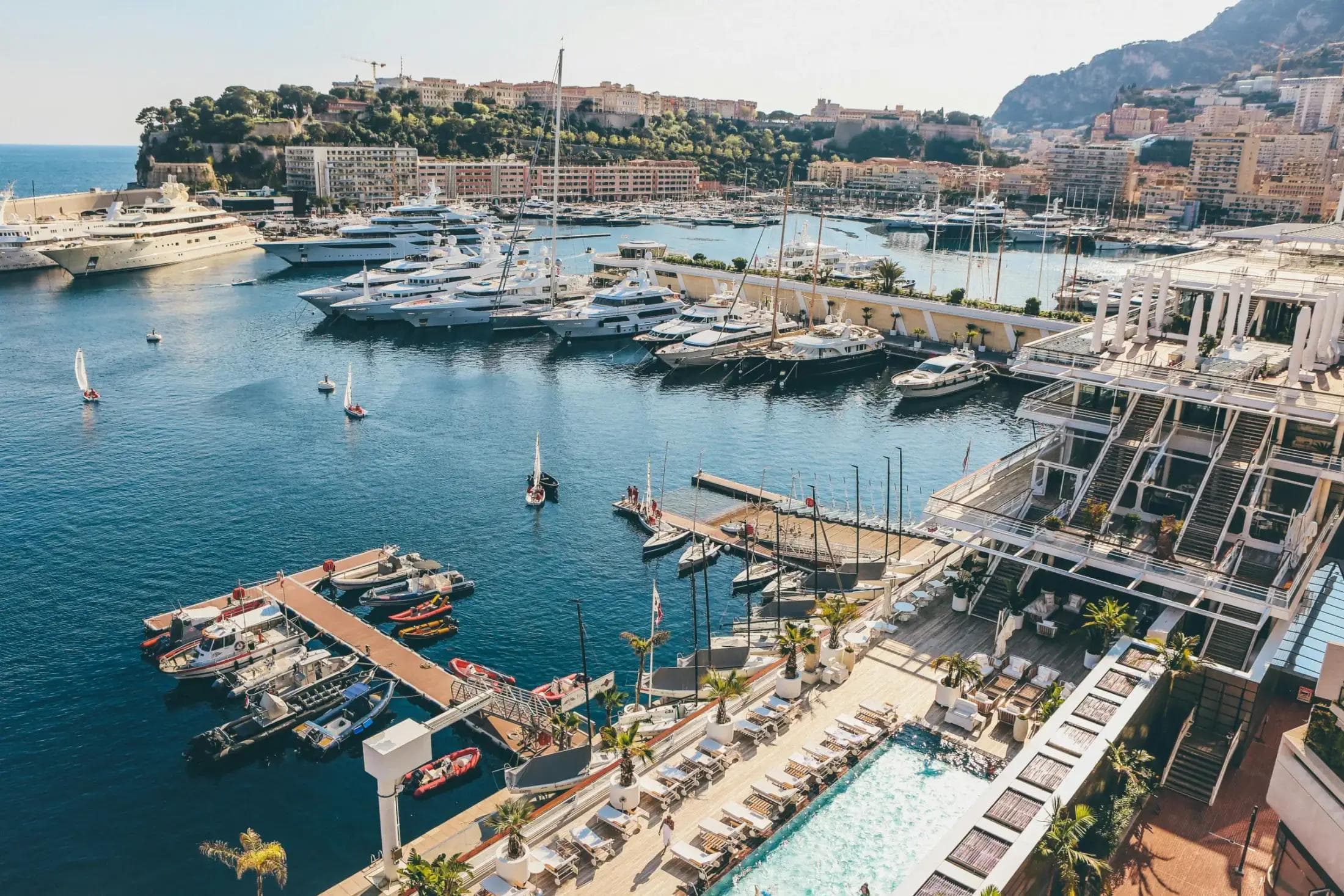Aerial view of Port Hercule in Monaco with multiple large superyachts moored at the docks on a clear spring day