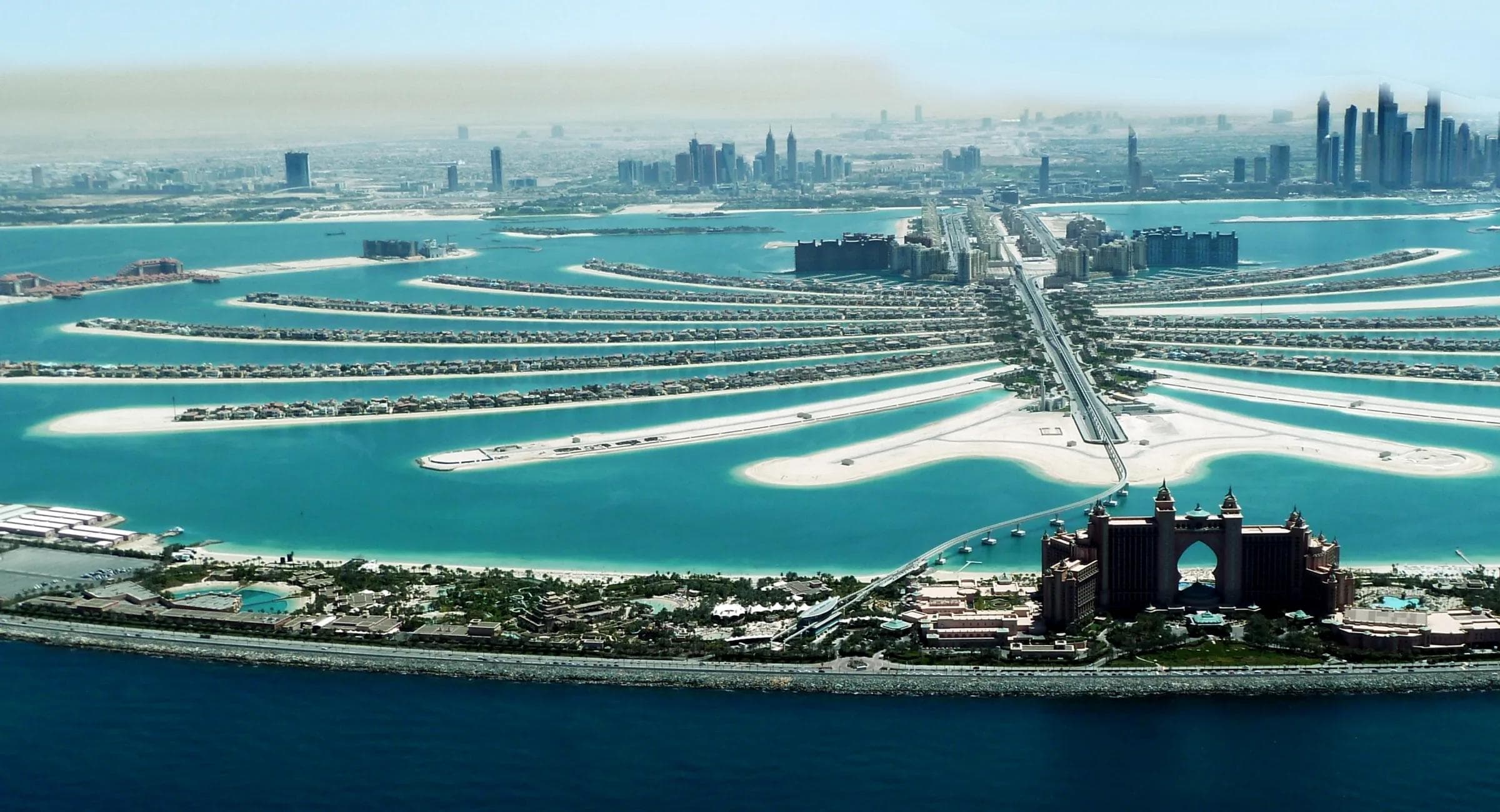 Aerial view of Palm Jumeirah, Dubai, showing the palm-shaped island with residential fronds, Atlantis hotel, and the Dubai Marina skyline on the horizon